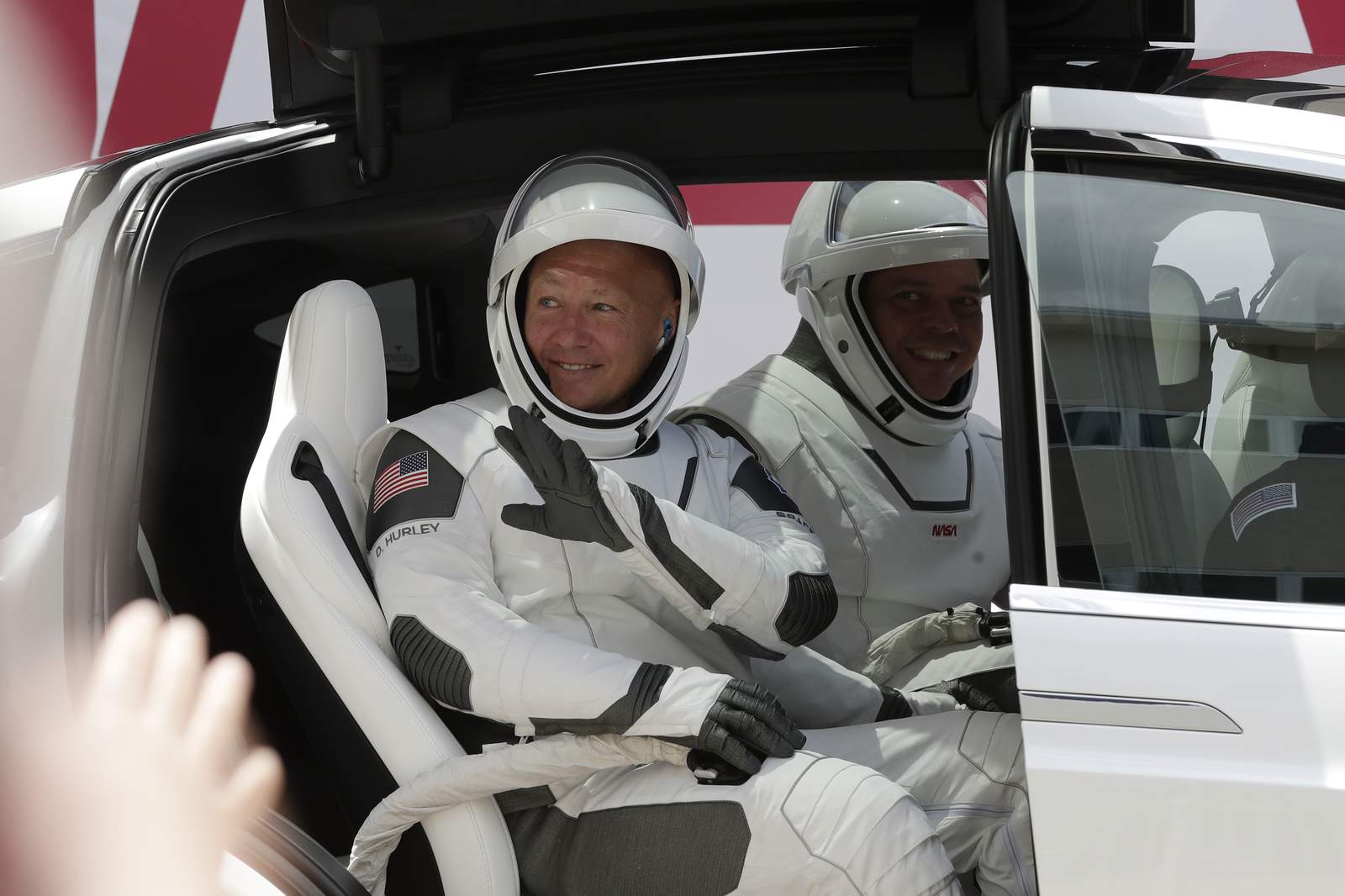 NASA astronauts Douglas Hurley, left, and Robert Behnken wave while seated in a Tesla SUV on their way to Pad 39-A, at the Kennedy Space Center in Cape Canaveral, Fla., Saturday, May 30, 2020. The two astronauts will fly on a SpaceX test flight to the International Space Station. For the first time in nearly a decade, astronauts will blast into orbit aboard an American rocket from American soil, a first for a private company. (AP Photo/John Raoux)